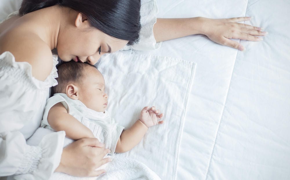 Ibu dan anak bayi sedang berbaring di kasur putih