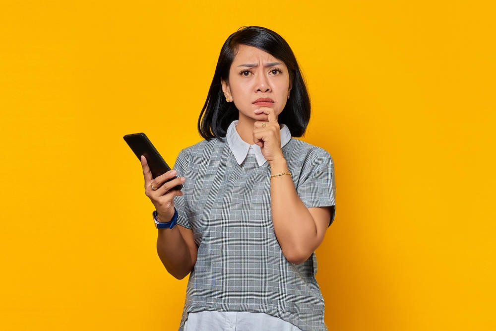 6 Tips Penting dalam Memilih Alat Kontrasepsi Seorang wanita sedang memegang dagu dan memegang handphone