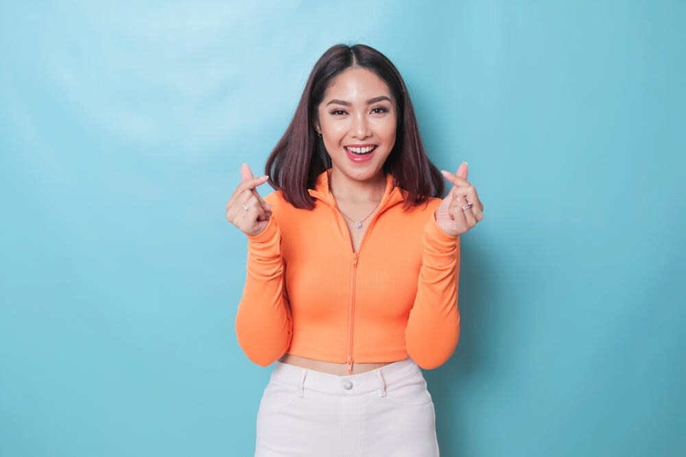 Wanita dengan Jari Tangan Hati dan Tersenyum Sumringah